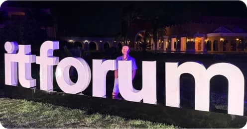 Letreiro “itforum” iluminado à noite, com uma pessoa ao fundo