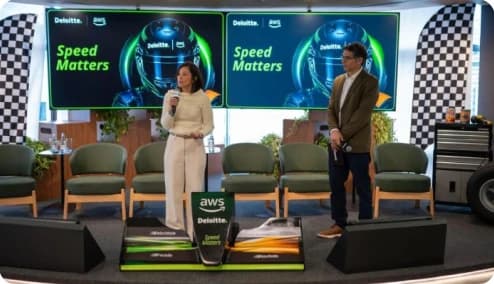 Palco do AI Symposium: Speed Matters, promovido pela Deloitte em parceria com a AWS, com duas pessoas conversando diante dos painéis